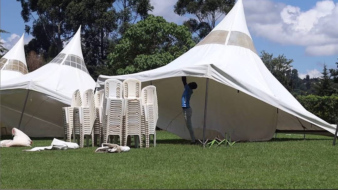 White peaked marquees being set up on the grounds with stacks of chairs